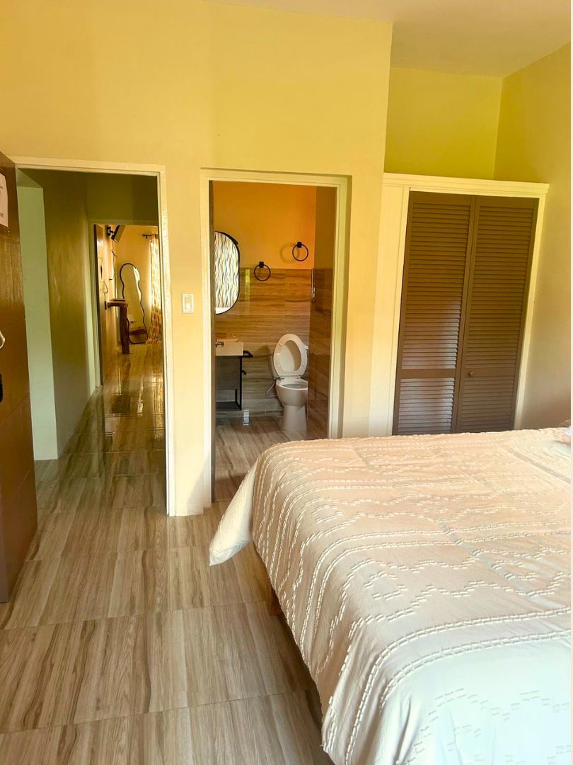 A bedroom with a bed, a bathroom with a toilet, and a hallway leading to a door.
