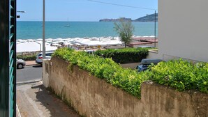 Vista costeira com rua pavimentada, carros estacionados e uma fileira de guarda-sóis brancos.