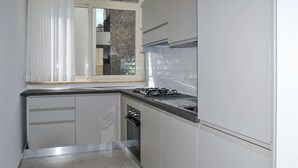 Cozinha compacta com armários brancos, fogão a gás e janela com persianas.