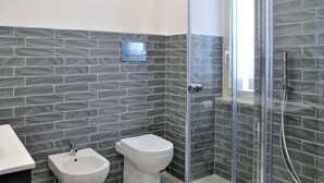 Casa de banho com design moderno, com cabine de duche com porta de vidro, um bidé e uma sanita.