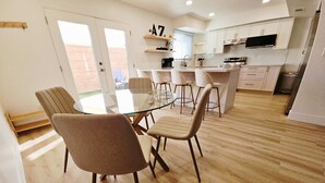A modern kitchen with white cabinets, a central island, and a glass dining table with chairs. - Osborn Oasis - Half a Mile to old Town and Hospital (Scottsdale)