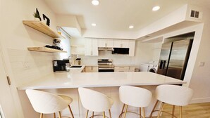 A modern kitchen with white cabinetry, a central island, and bar stools. - Osborn Oasis - Half a Mile to old Town and Hospital (Scottsdale)