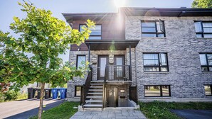 A modern two-story building with a brick facade, a central entrance with a staircase, and a tree in the foreground. - 1756 Rue Balmoral | 3BR / 1BA Modern City Retreat (Longueuil)