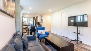 A modern living room with a leather sofa, a blue armchair, a coffee table, and a flat-screen TV mounted on the wall. - 1756 Rue Balmoral | 3BR / 1BA Modern City Retreat (Longueuil)