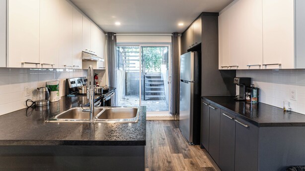 A modern kitchen with a stainless steel sink, a coffee maker, and a refrigerator. - 1756 Rue Balmoral | 3BR / 1BA Modern City Retreat (Longueuil)