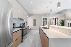 Een moderne keuken met roestvrijstalen apparatuur, een groot eiland met een spoelbak en hangende lampen.