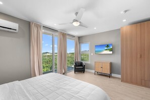 A bedroom with a large bed, a ceiling fan, an air conditioning unit, a TV, and a view of a beach through large windows. - Gorgeous 3-bedroom Villa with AC, Pool/Hot Tub in Cooper Jack Bay Settlement (Cooper Jack Bay Settlement)