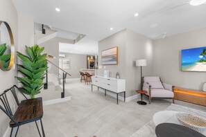 A modern interior with a staircase, a dining area, a living room with a sofa and a TV, and a kitchen in the background. - Gorgeous 3-bedroom Villa with AC, Pool/Hot Tub in Cooper Jack Bay Settlement (Cooper Jack Bay Settlement)