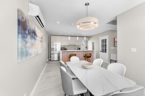 Cozinha moderna com eletrodomésticos de aço inoxidável, área de jantar com mesa de mármore e uma grande pintura abstrata na parede.