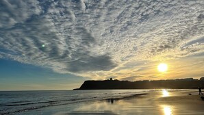 En strand ved solnedgang, roligt vand og en fjern bakke.