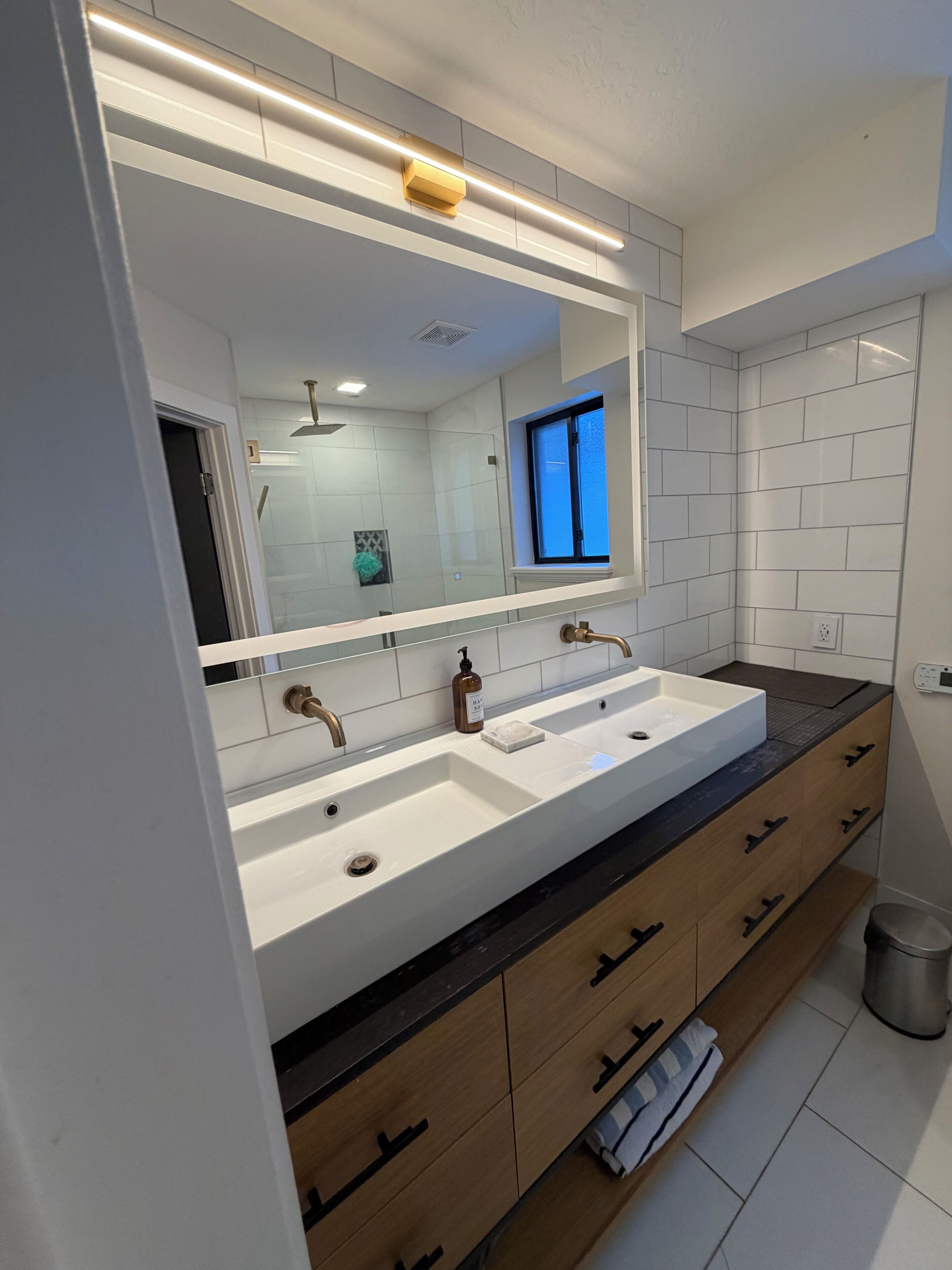 Un baño moderno con lavamanos doble, armarios de madera y un espejo grande.