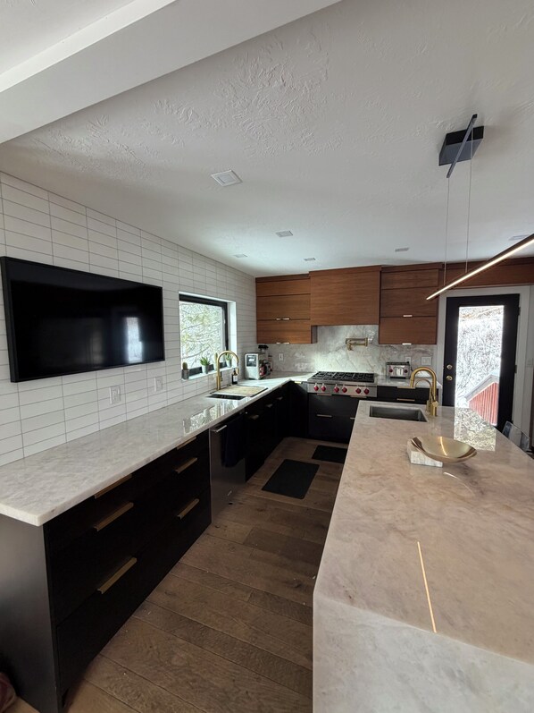 Una cocina moderna con una isla grande, armarios oscuros, azulejos blancos tipo metro y un televisor integrado.