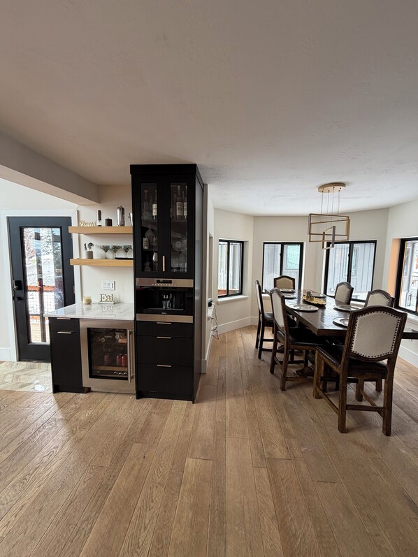 Een moderne keuken met een ingebouwde wijnrek, een eethoek met een houten tafel en stoelen, en grote ramen die natuurlijk licht binnenlaten.