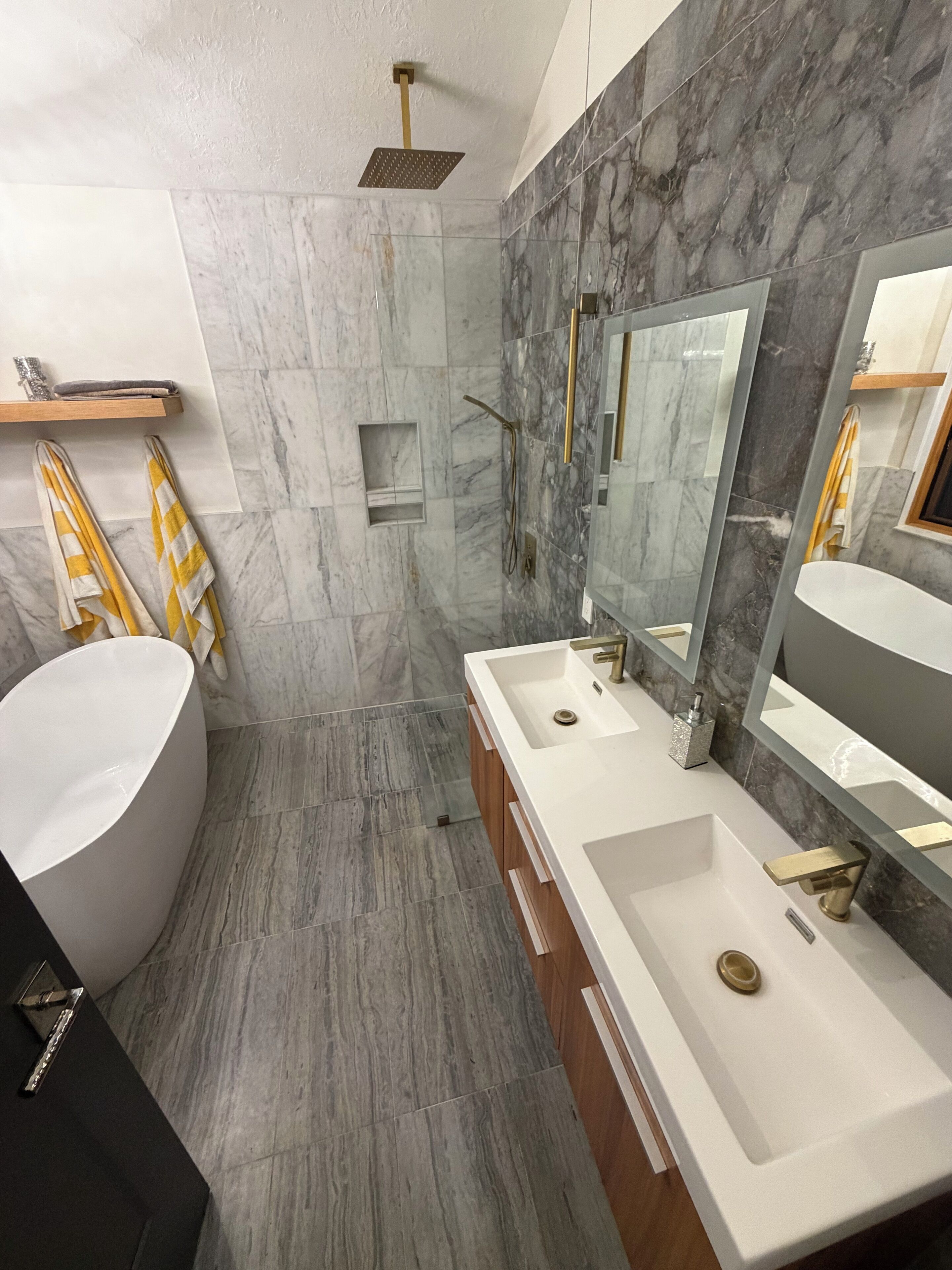 A modern bathroom with a freestanding bathtub, two sinks with mirrors, a shower area, and marble walls.