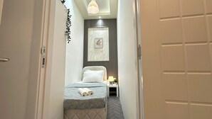A narrow hallway leading to a bedroom with a bed, a nightstand, a wall-mounted picture, and a ceiling light. - Atelier Partition Room in Tecom  (Dubai)
