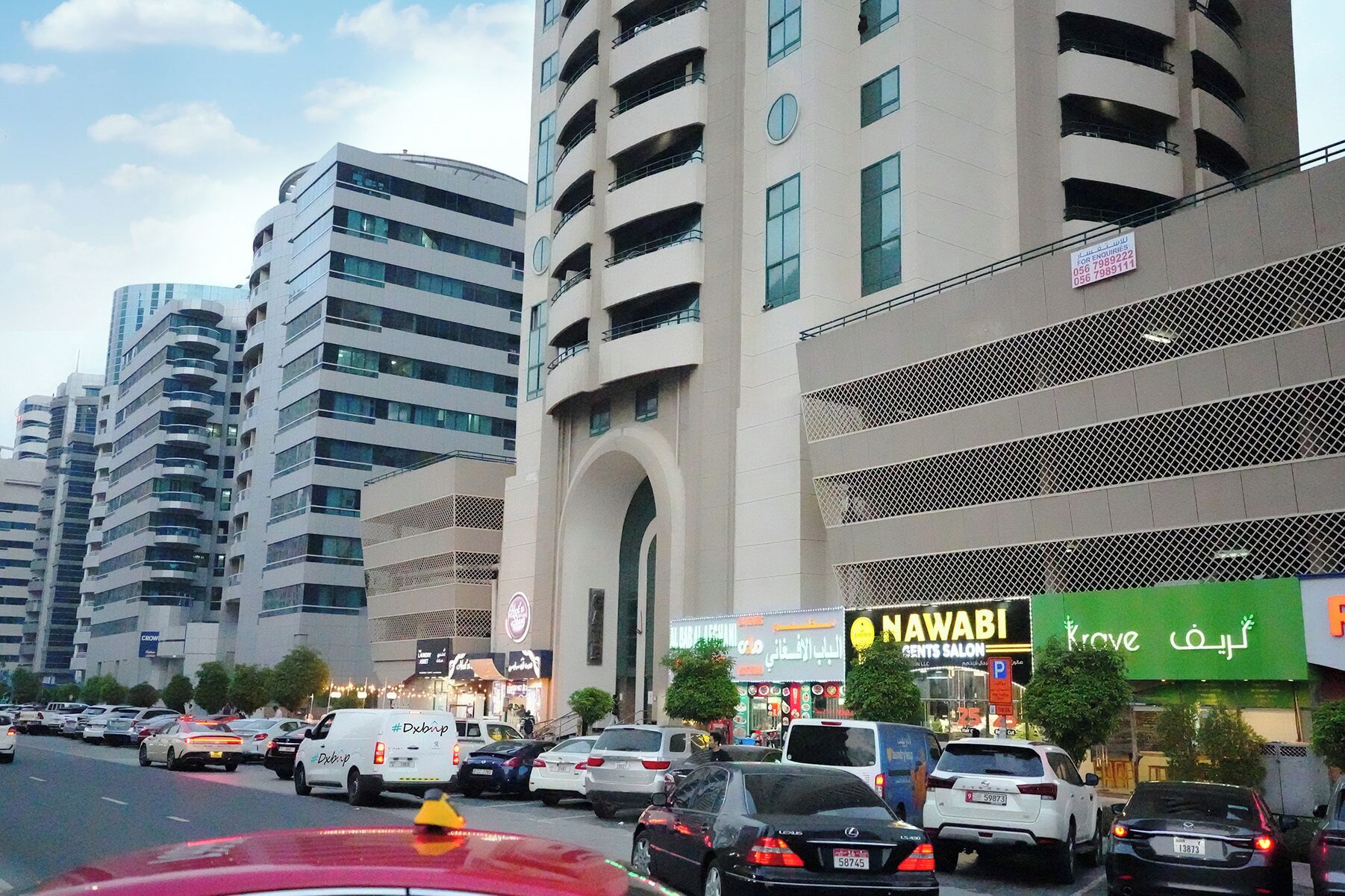 A busy urban street with modern buildings, a prominent archway, and various commercial establishments including a men's salon.
