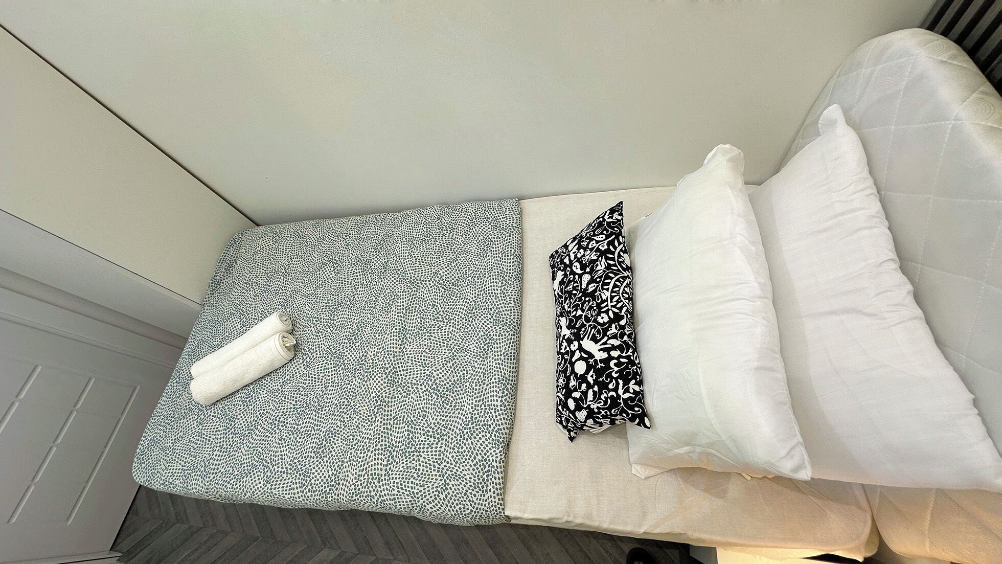Un lit bien fait, avec une literie à motifs, une serviette enroulée et un oreiller.