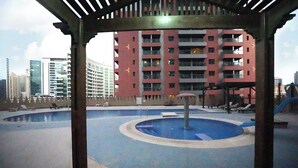 A rooftop pool area with a circular water feature, surrounded by lounge chairs and a pergola structure. - Atelier Partition Room in Tecom  (Dubai)