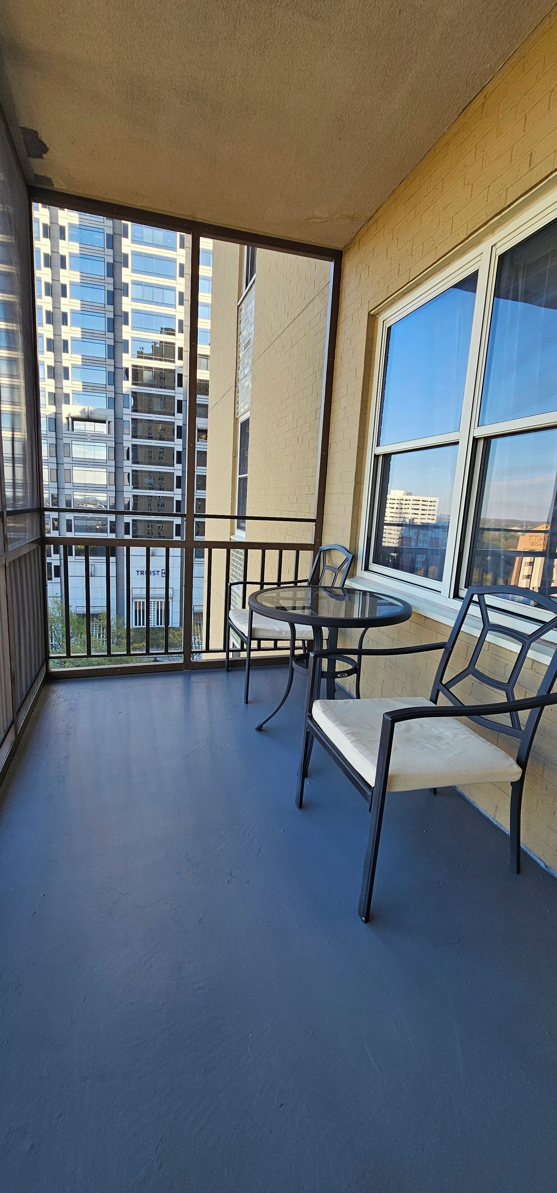 A balcony with a table and chairs, a view of tall buildings, and a brick wall.