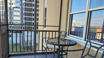 A balcony with a table and chairs, a view of tall buildings, and a brick wall.