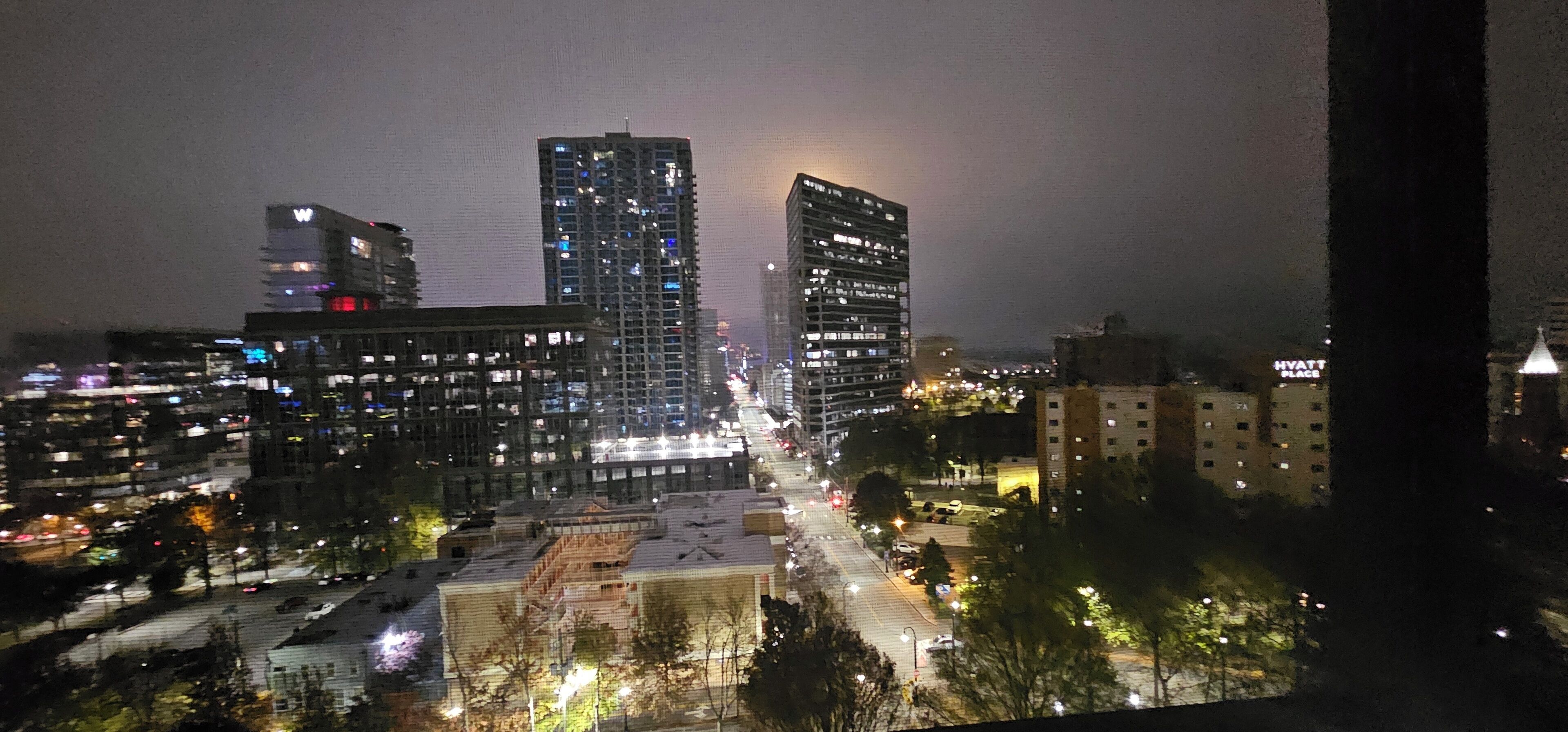 A nighttime cityscape with high-rise buildings, illuminated windows, and a busy street.