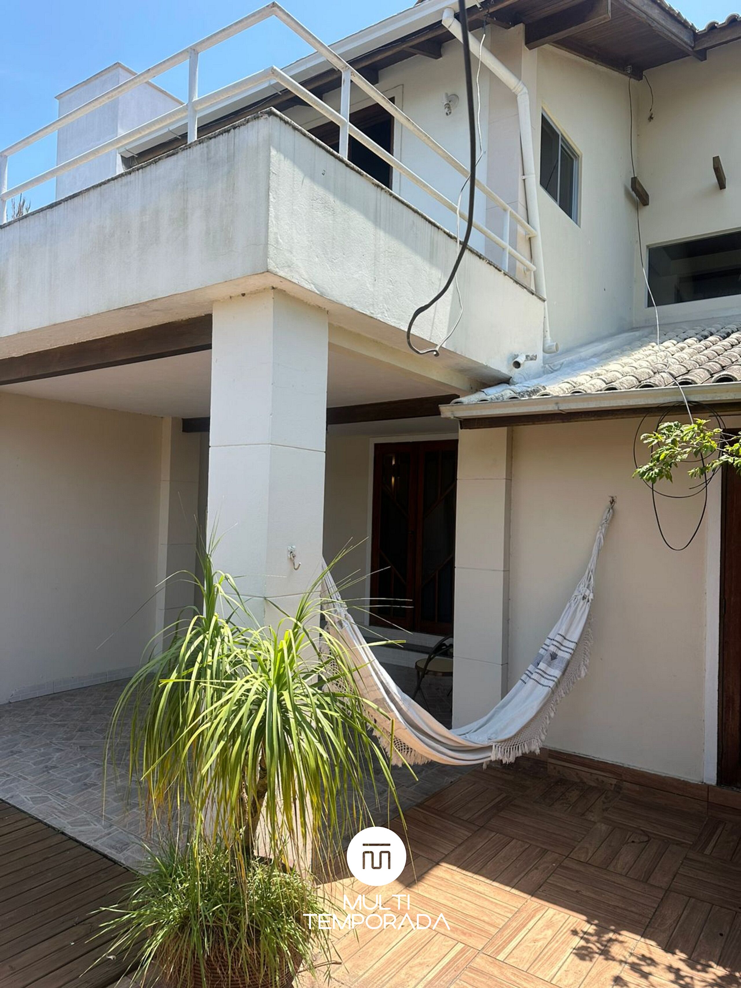 A two-story building with a balcony, a hammock, and a potted plant.
