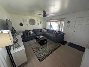 A modern living room with a sectional sofa, a coffee table, a standing lamp, and a ceiling fan.