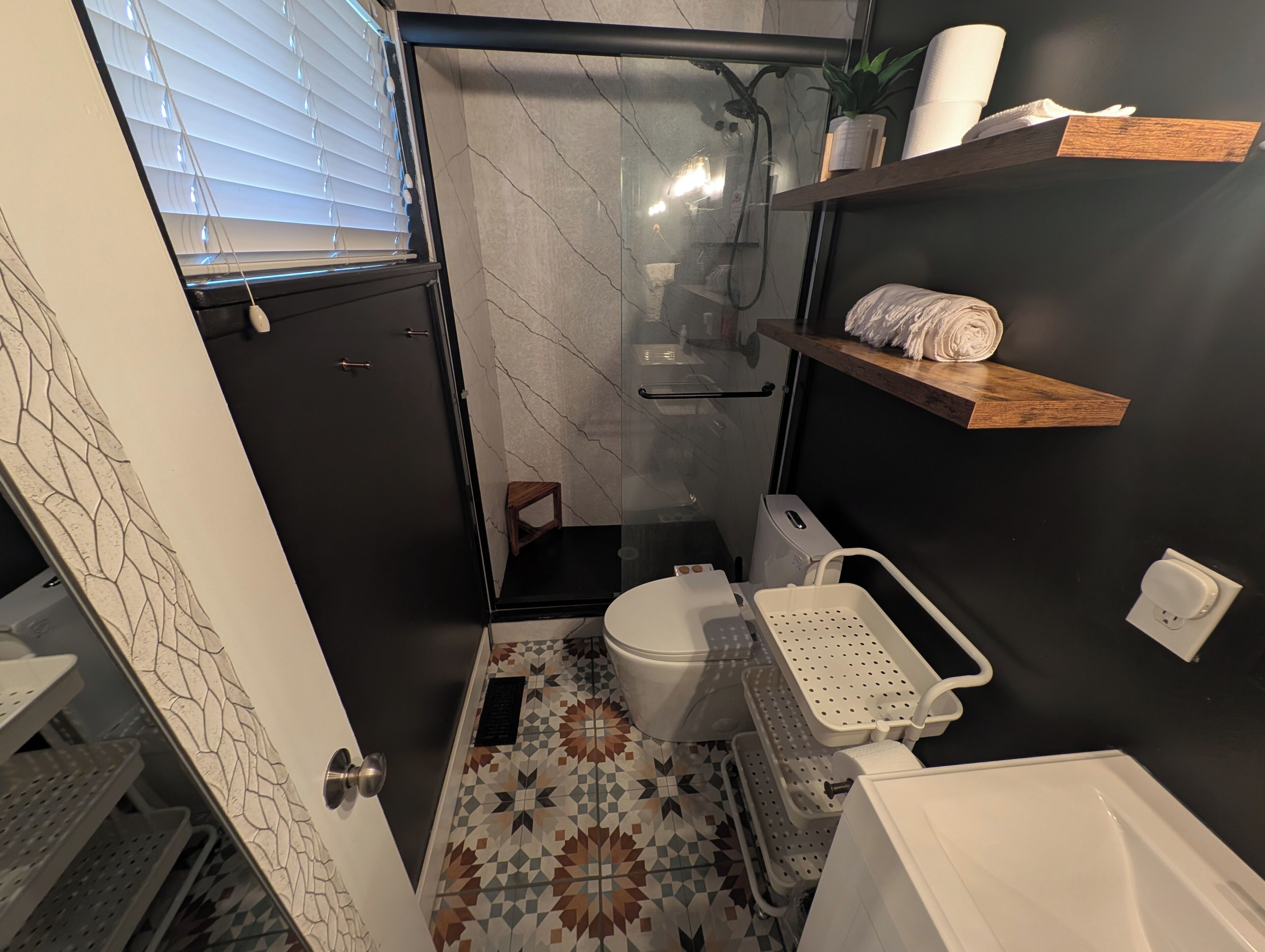 A compact bathroom with a toilet, shower, and storage shelves.