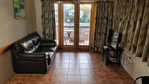 A living room with a leather sofa, a television, and a sliding glass door leading to an outdoor patio. - Cairns holiday unit apartment kitchen aircon wifi near esplanade and hospital (Cairns North)