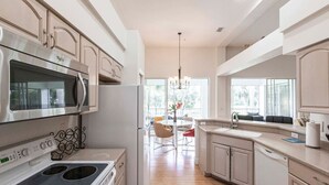 Una cocina moderna con electrodomésticos de acero inoxidable, un comedor con candelabro y ventanas grandes.