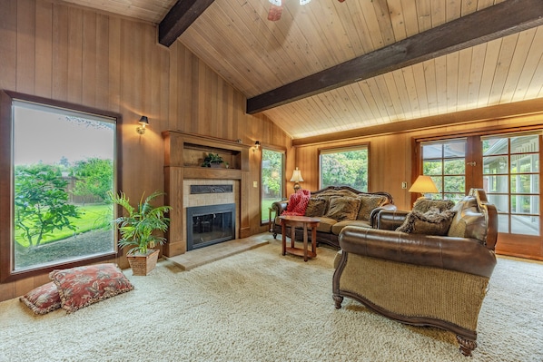 A cozy living room with a fireplace, leather sofa, and large windows offering a view of the outdoors.