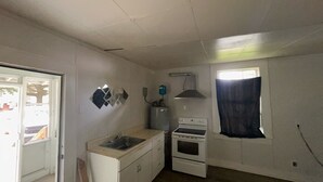 Una cocina pequeña con un lavamanos, estufa y ventana con cortina.