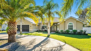 A single-story house with a garage, a front yard with a palm tree, and a well-maintained lawn. - 4BR Family Retreat with Pool, Lanai, Bikes & Games (Palm Coast)