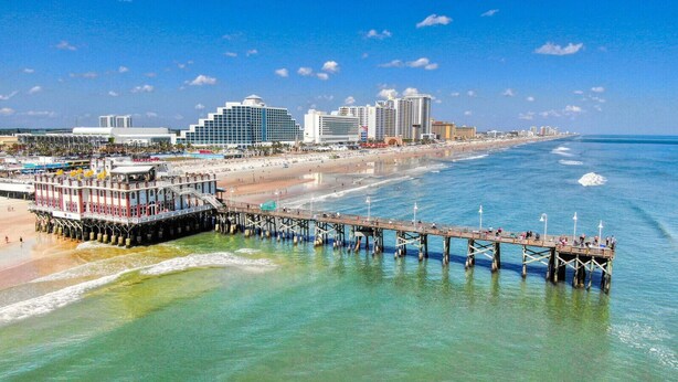 A pier extending into the ocean with a building at the end, a beach, and a city skyline in the background. - 4BR Family Retreat with Pool, Lanai, Bikes & Games (Palm Coast)