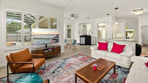 A modern living room with a television, a white sofa with red cushions, a brown leather chair, and a wooden coffee table. - 4BR Family Retreat with Pool, Lanai, Bikes & Games (Palm Coast)