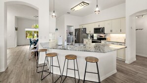 A modern kitchen with a large island, bar stools, stainless steel appliances, and pendant lighting. - 4BR Family Retreat with Pool, Lanai, Bikes & Games (Palm Coast)