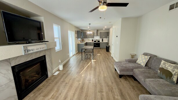 A modern living room with a fireplace, a flat-screen TV, and a sofa. There is a kitchen in the background with cabinets and a dining area. - Modern Luxe Haven. Close to the airport, military bases, and downtown (Colorado Springs)