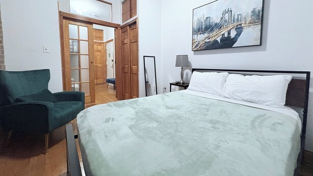 Ein Hotelzimmer mit einem Bett, einem Sessel, einem Stadtbild und einer Tür zu einem weiteren Raum.
