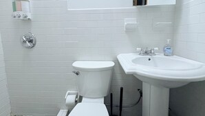 Ein Badezimmer mit weißen Fliesen, einer Toilette, einem Waschbecken und einem Spiegel.