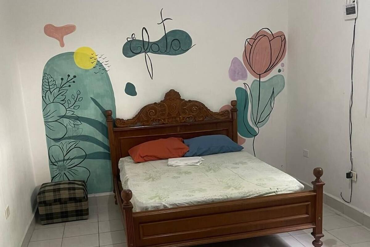 Et soveværelse med en træseng, en ternet taske, og en væg med blomster- og abstrakte motiver.