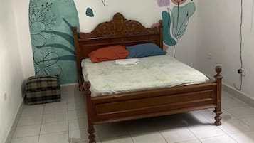 A bedroom with a wooden bed, a plaid bag, and a wall with floral and abstract designs.