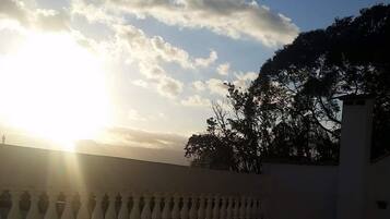 Un balcon orné d’une balustrade, un ciel dégagé et le soleil se couchant ou se levant.