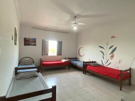 Une pièce comprenant quatre lits en bois disposés en forme de U, un ventilateur de plafond, une fenêtre avec des stores et un mur orné d’une fresque florale.