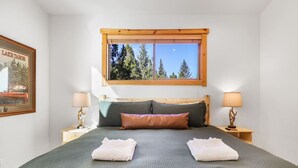 Una camera da letto con un letto grande, due comodini, una finestra vista alberi e un quadro appeso al muro.