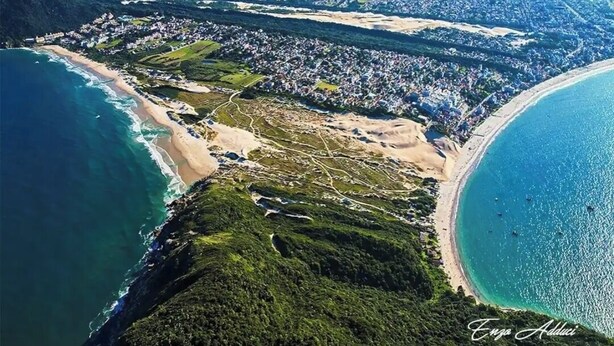 Luftaufnahme einer Küstenstadt mit Strand, Wohngebieten und Bergen im Hintergrund.
