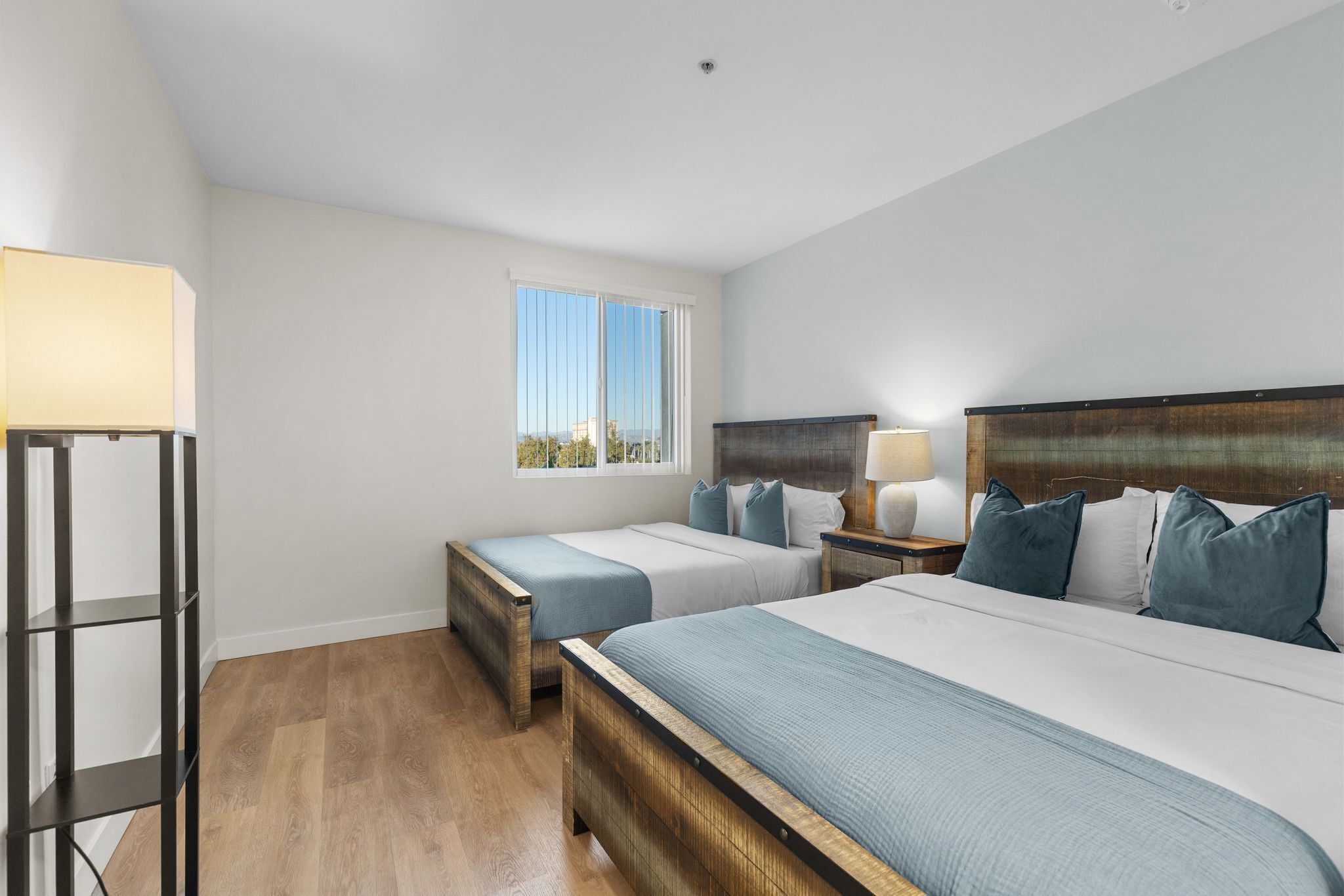 A bedroom with two beds, a bedside table, a lamp, and a window.