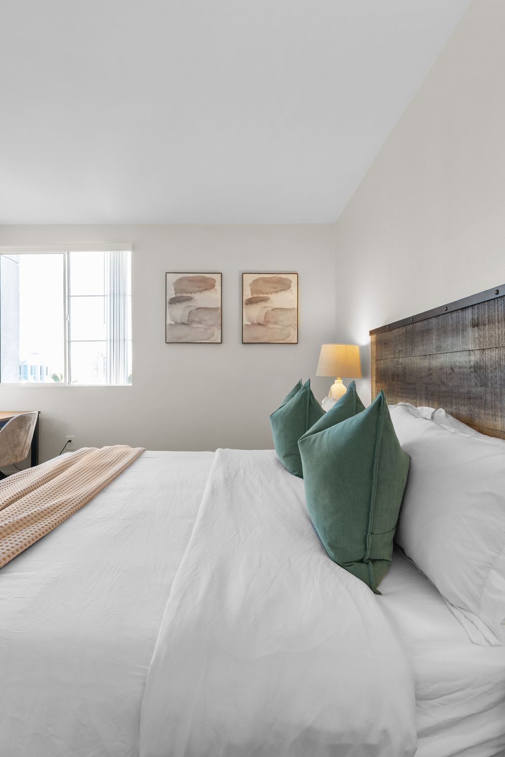 Habitación de hotel con una cama grande, dos cuadros en la pared, una lámpara de noche y vistas de la ciudad a través de la ventana.