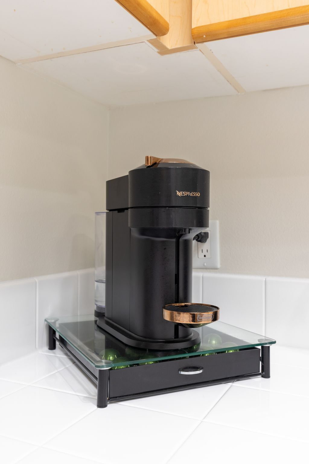 Une machine à café Nespresso noire, dotée d’un réservoir d’eau en verre, posée sur un comptoir blanc recouvert de carreaux.