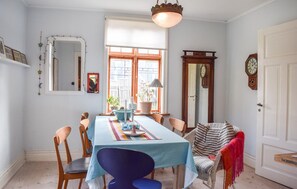 En spisestue med et bord dækket til fire personer, stole, en hængende lysekrone, et spejl og et ur på væggen.