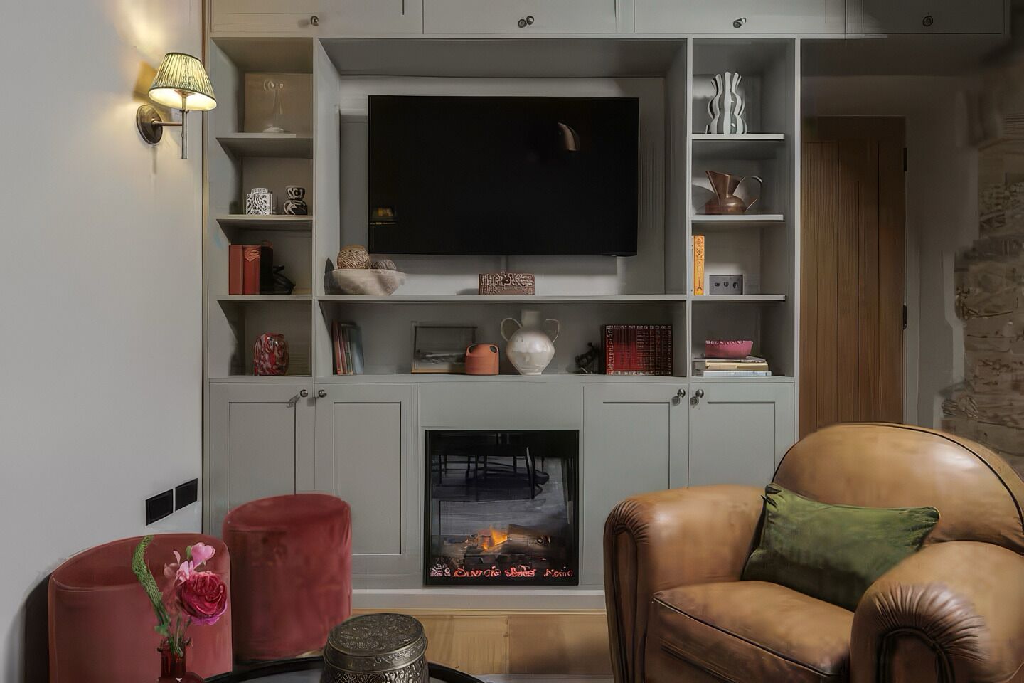 Una sala de estar con chimenea, televisor montado encima y un sillón de cuero con cojín verde.